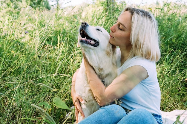 Une femme avec un chien golden retriever joue et se serre dans l'herbe.