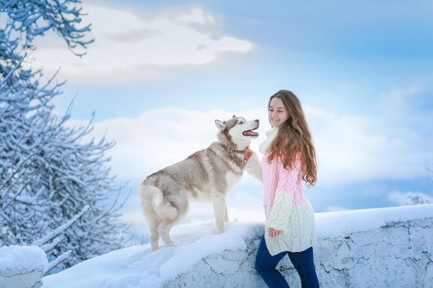 Une femme avec un chien husky marchant sur les montagnes enneigées d'hiver
