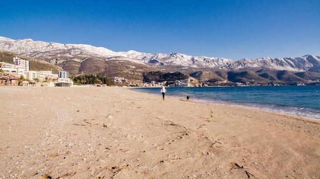 Femme avec le chien sur la plage en hiver. Montagnes en arrière-plan de neige.