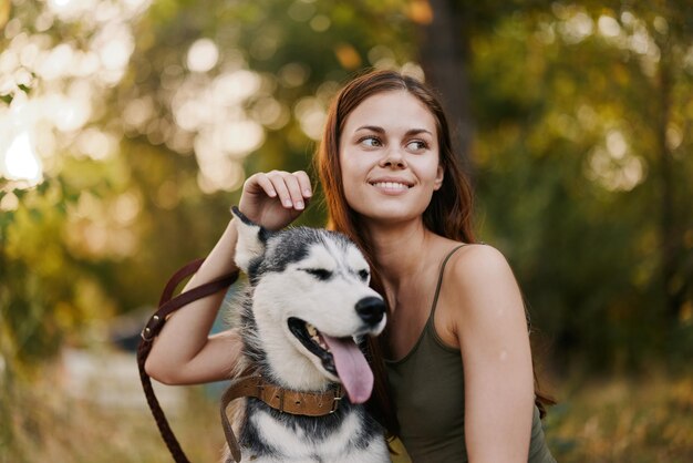 Une femme avec un chien de race husky sourit et caresse affectueusement son chien bien-aimé en se promenant dans la nature dans le parc en automne sur fond de coucher de soleil