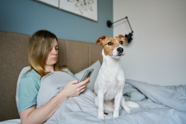 Femme avec chien se détendre sur le lit utiliser un smartphone