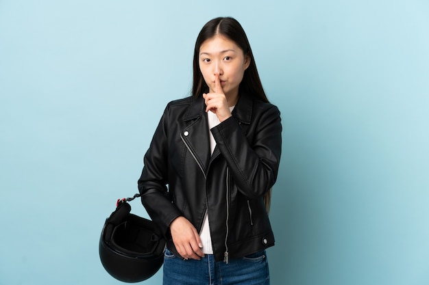 Femme chinoise tenant un casque de moto sur bleu faisant le geste de silence