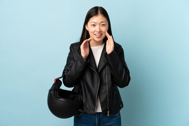 Femme chinoise tenant un casque de moto sur un mur bleu isolé en criant avec la bouche grande ouverte