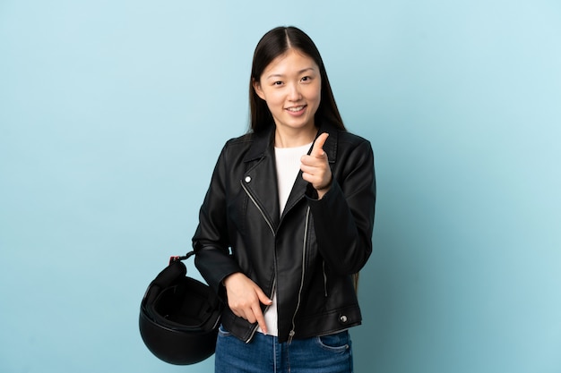 Femme chinoise tenant un casque de moto sur le mur bleu pointe le doigt vers vous