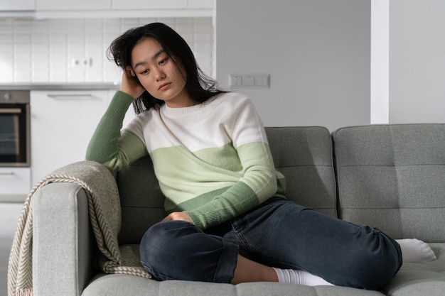 Une femme chinoise triste et agacée est assise sur le canapé et souffre de dépression après avoir rompu avec son petit ami.