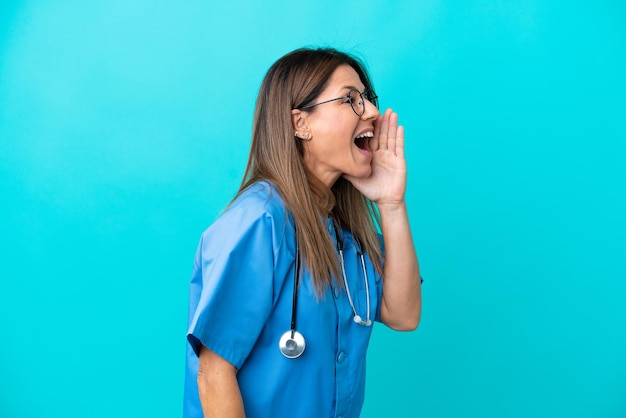 Femme chirurgien d'âge moyen isolée sur fond bleu criant avec la bouche grande ouverte sur le côté