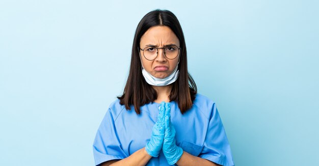 Femme chirurgien sur le mur bleu maintient la paume ensemble.