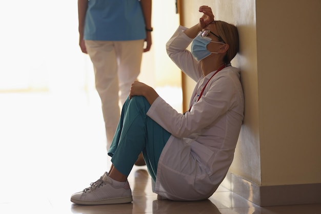 Une femme chirurgienne expire après une longue opération assise dans le couloir de la clinique sur le sol