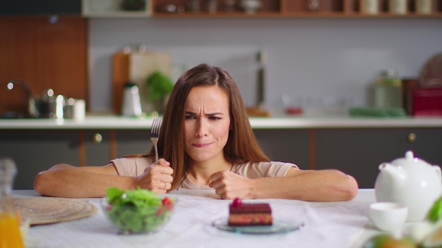 Femme choisissant une salade au lieu d'un gâteau dans la cuisine Fille avec une fourchette essayant une salade fraîche
