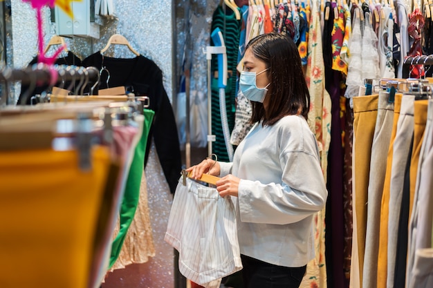 Femme choisissant des vêtements au centre commercial et portant un masque médical pour la prévention du coronavirus