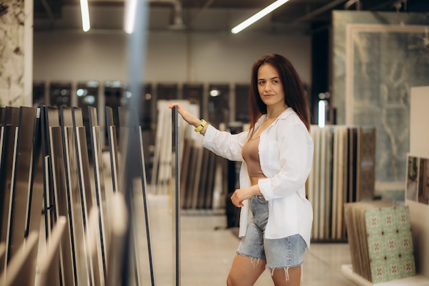 Une femme choisit des carreaux de céramique dans une quincaillerie Une belle blonde dans une veste noire touche des échantillons dans une vitrine Réparation et design d'intérieur