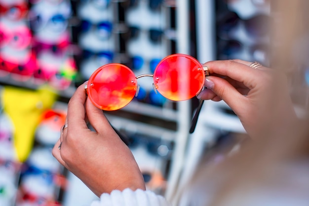 Une femme choisit des lunettes de soleil de protection dans le contexte d'une vitrine avec des lunettes.