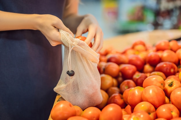 Une femme choisit des tomates dans un supermarché sans utiliser un sac en plastique réutilisable pour acheter