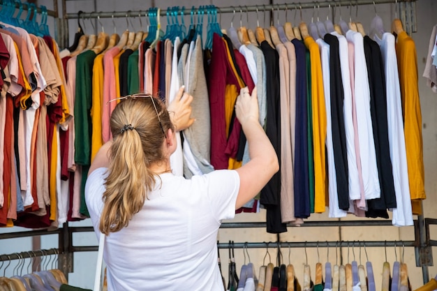 la femme choisit des vêtements en passant par le diffuseur dans le magasin du marché. vue arrière