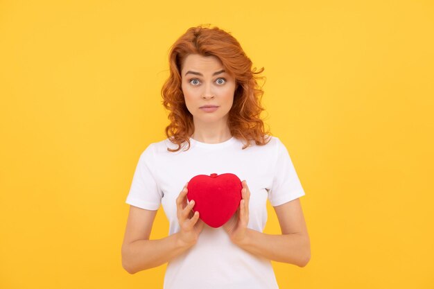 Femme choquée présentant un coeur rouge sur fond jaune chérie