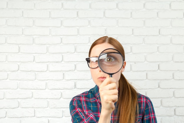 Femme choquée regardant à travers une loupe.