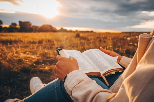 Une femme chrétienne tient la bible dans ses mains Lire la Sainte Bible dans un champ pendant un beau coucher de soleil Concept pour la foi, la spiritualité et la religion Espoir de paix