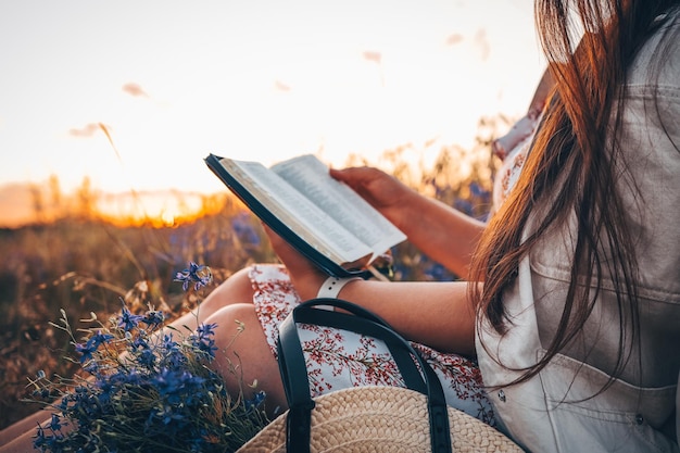 Une femme chrétienne tient la bible dans ses mains Lire la Sainte Bible dans un champ pendant un beau coucher de soleil Concept pour la foi, la spiritualité et la religion Espoir de paix