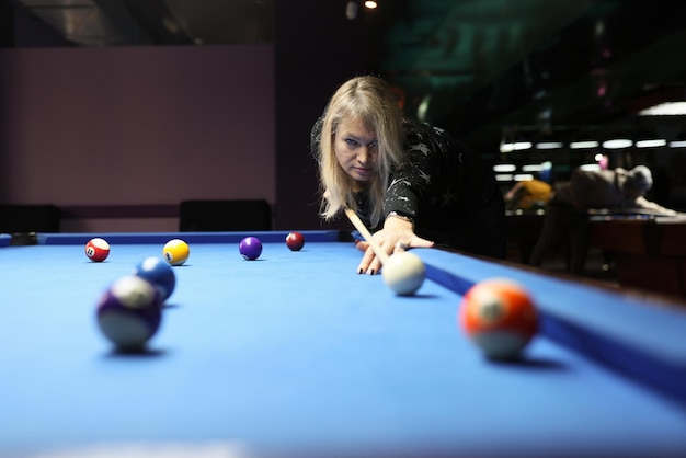 Une femme ciblée frappe une balle blanche penchée au-dessus d'une table de billard bleue une femme blonde aime jouer