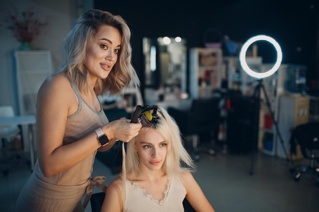 Femme de coiffeur faisant des extensions de cheveux à la jeune femme aux cheveux blonds en extension de cheveux professionnels de salon de beauté