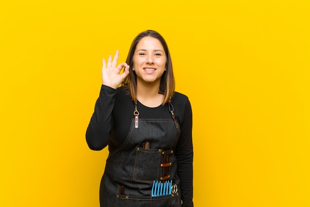 Femme coiffeur se sentir heureux, détendu et satisfait, montrant l'approbation avec le geste correct, souriant sur fond orange