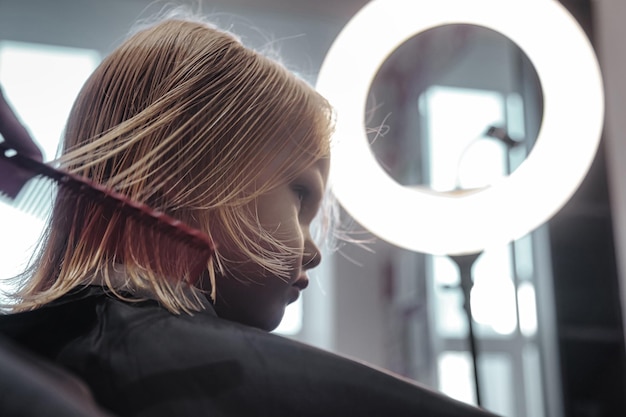 Une femme coiffeuse fait une jolie coiffure à la mode pour une petite fille mignonne