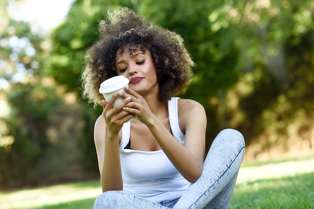 Femme avec une coiffure afro, boire du café dans le parc