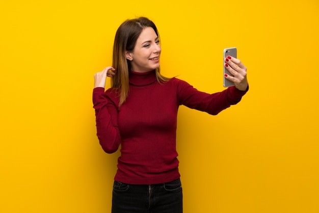 Femme avec col roulé sur mur jaune faisant un selfie