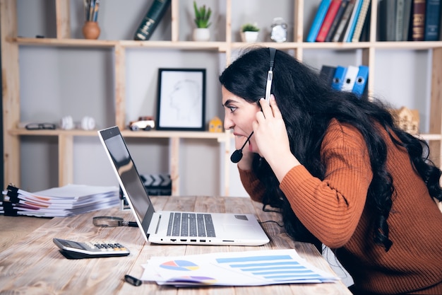 Femme en colère dans un casque et un ordinateur au bureau