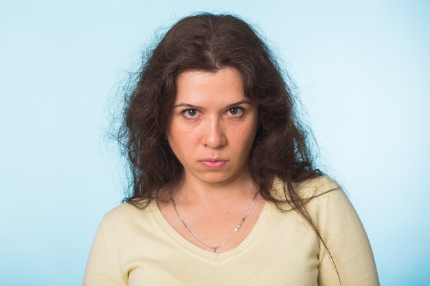 Femme en colère regarde la caméra, beau visage de femme sur bleu