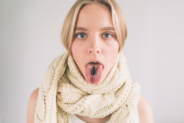 Femme collant sa langue avec une pilule noire dessus.