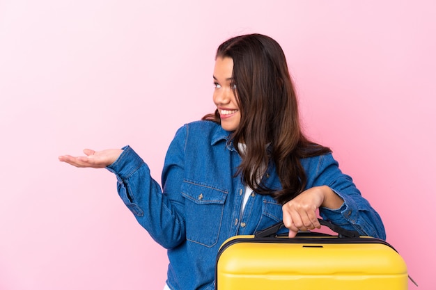 Femme colombienne voyageur tenant une valise sur un mur rose isolé avec une expression faciale surprise