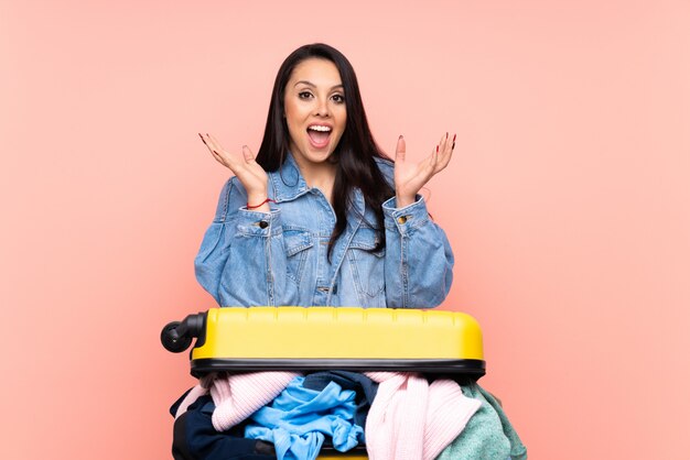 Femme colombienne voyageur avec une valise pleine de vêtements sur le mur rose isolé malheureux et frustré par quelque chose