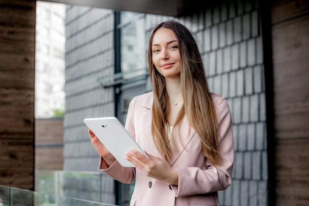 Femme commerçante en costume souriant tenant une tablette et regardant la caméra