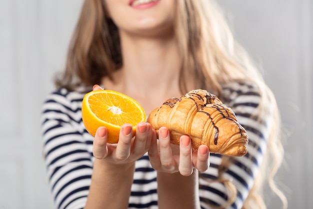 Femme, comparaison, gâteau malsain, fruit orange