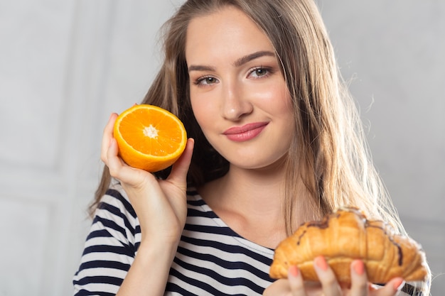 Femme, comparaison, gâteau malsain, fruit orange