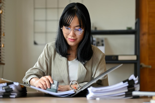 Femme comptable asiatique travaillant à son bureau à l'aide d'un tampon en caoutchouc pour approuver un projet