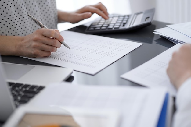 Femme comptable utilisant une calculatrice et un ordinateur portable tout en comptant les taxes pour un client. Concepts d'audit d'entreprise