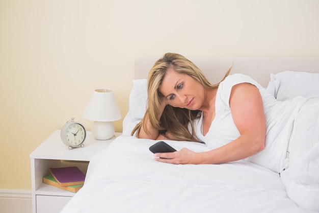 Femme concentrée à l&#39;aide d&#39;un téléphone portable allongée sur son lit