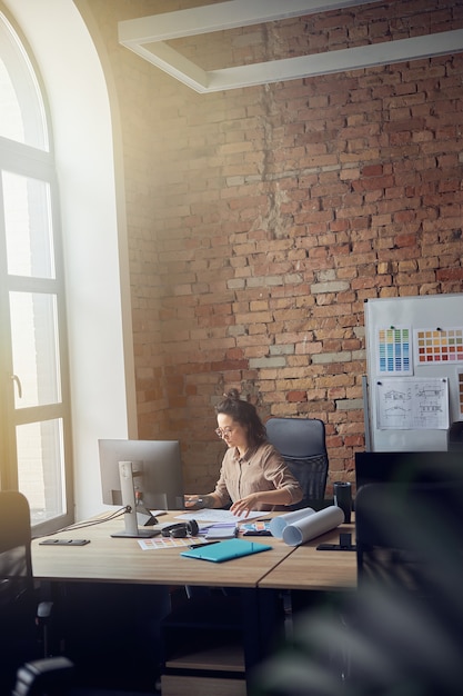 Femme concentrée dans des verres architecte ou designer professionnel travaillant sur un plan assis à