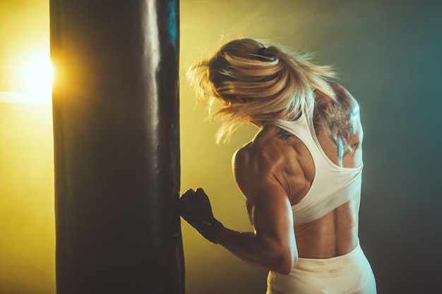 Femme concentrée faisant une séance d'entraînement de boxe fitness avec un sac de boxe.