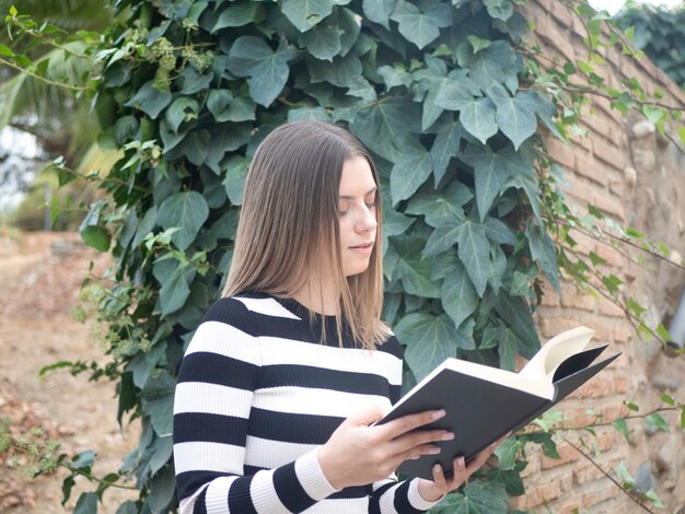 Femme concentrée lisant un roman intéressant contre le lierre