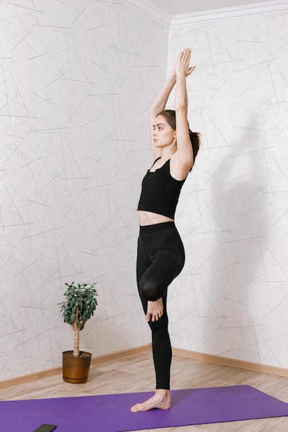 femme concentrée paisible debout dans la pose de l'arbre avec les bras levés et pratiquant le yoga