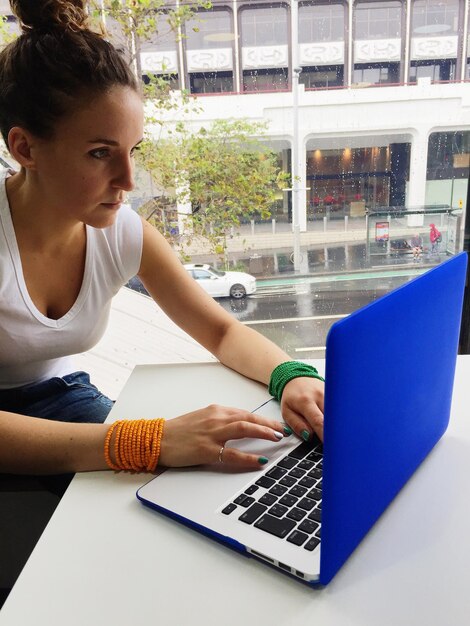 Photo femme concentrée utilisant un ordinateur portable par une fenêtre en verre