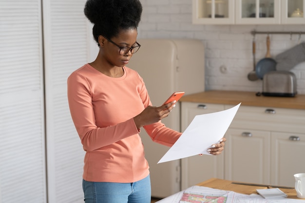 Une femme conceptrice à distance du millénaire prend une photo d'un document sur un smartphone pour envoyer un plan au client ou au patron