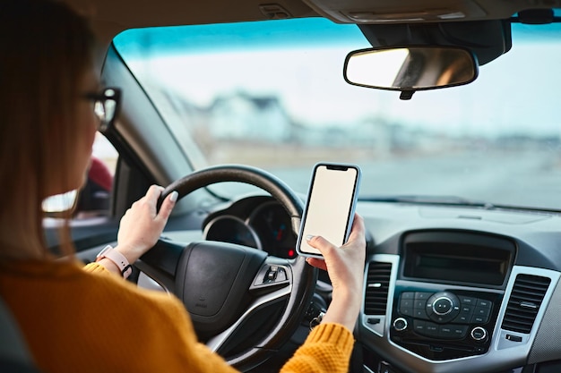 Femme conductrice utilisant une maquette vierge d'écran de téléphone portable sur la route tout en conduisant une voiture