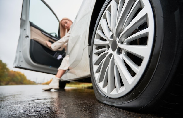 Photo femme conductrice de voiture blanche observant un pneu crevé sur la roue arrière