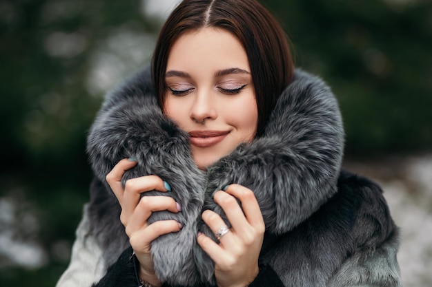 Femme confiante de mode posant à l'extérieur de la rue habillée d'un manteau de fourrure artificielle en vacances d'hiver