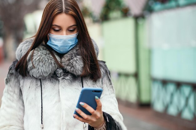 Une femme confiante se tient à l'extérieur du téléphone, porte un masque jetable bleu pour se protéger contre le virus