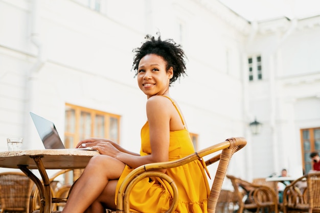 Une femme confiante sourit alors qu'elle est assise dans un café d'été Un étudiant apprend en ligne sur un ordinateur portable